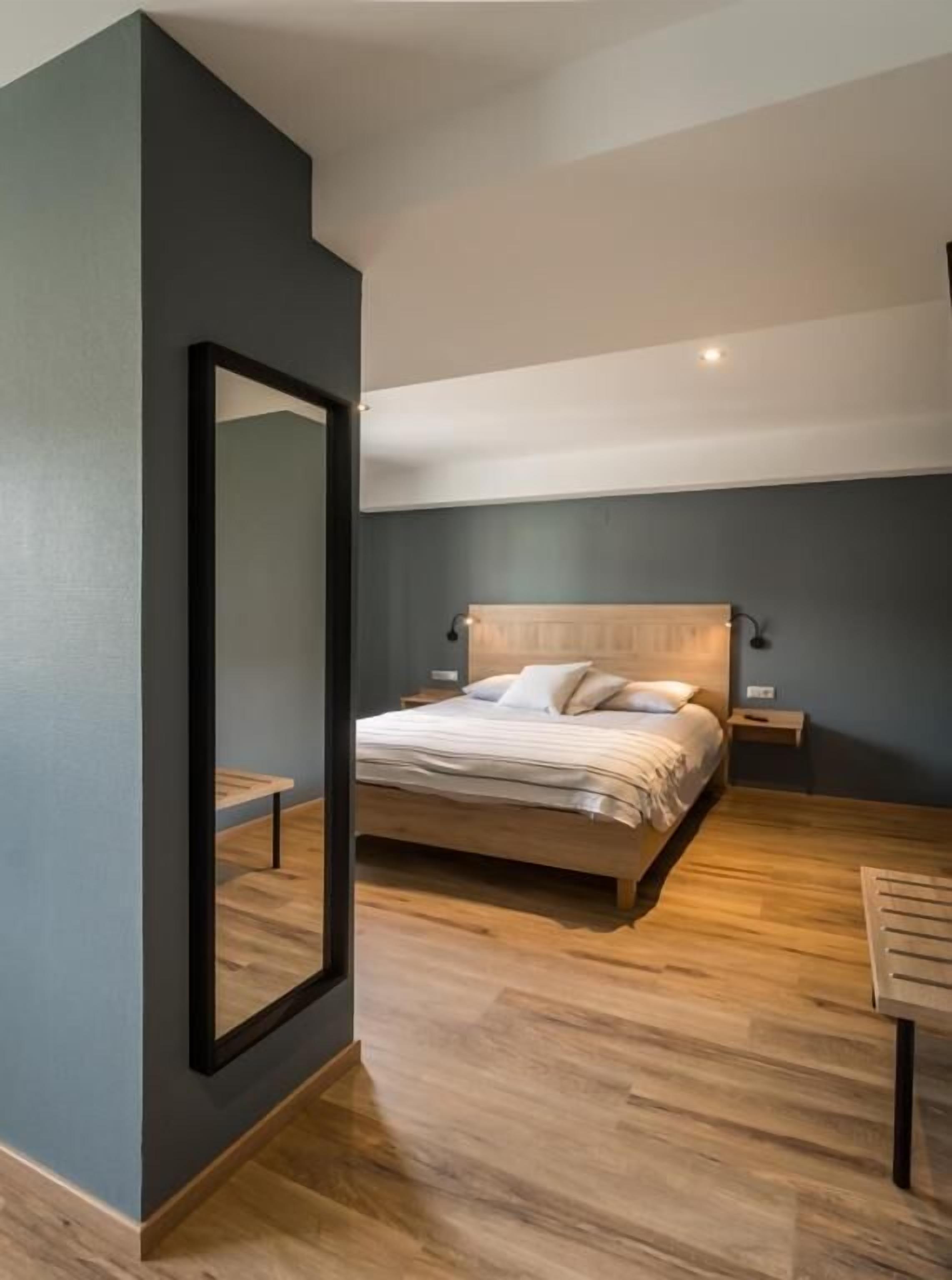 Une chambre moderne avec un grand lit, une tête de lit en bois, des tables de chevet et un miroir.