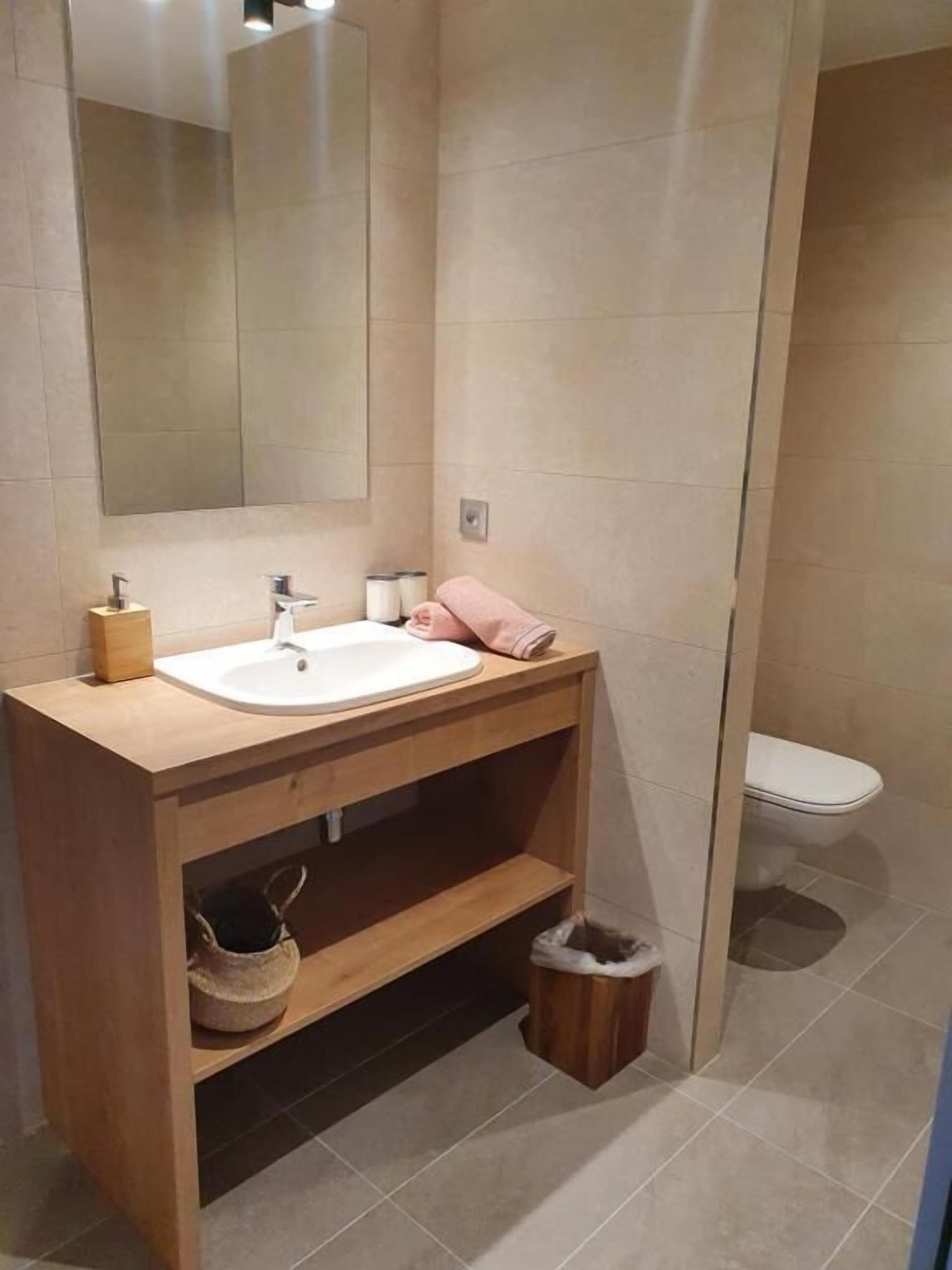 Une salle de bain moderne avec un meuble-lavabo en bois, un grand miroir et des toilettes.
