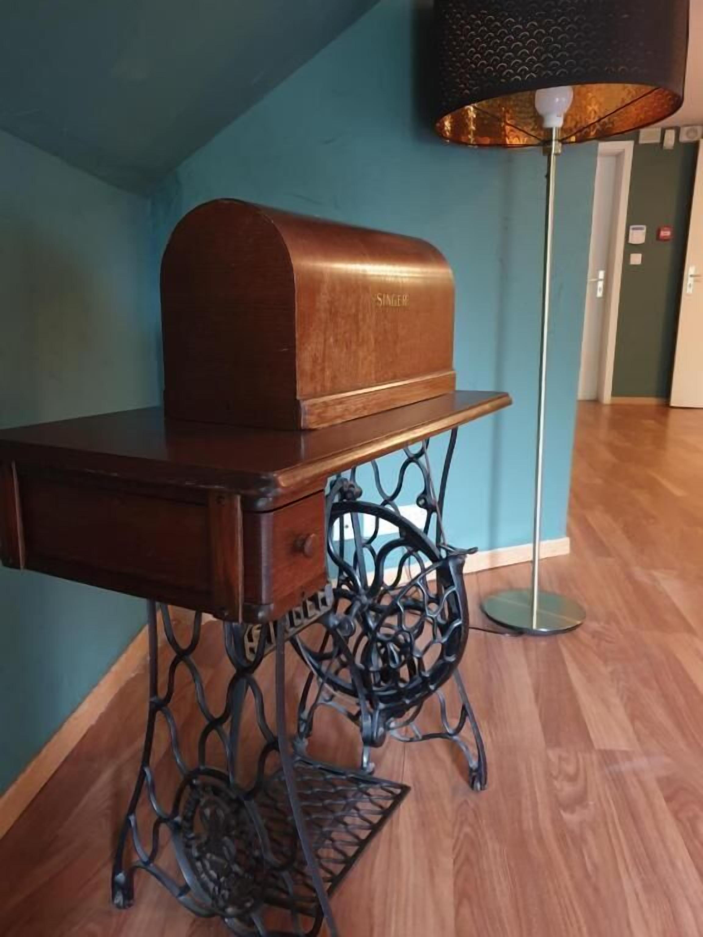 Una panca di legno con base metallica e un piccolo cassetto, davanti a una parete color petrolio e un pavimento in legno.