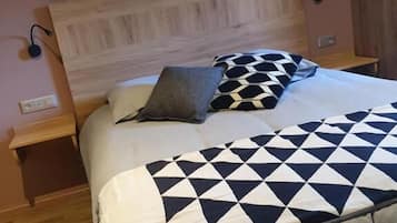 A bedroom with a wooden headboard, a bed with a geometric patterned bedspread, two bedside tables, and a wall-mounted lamp.