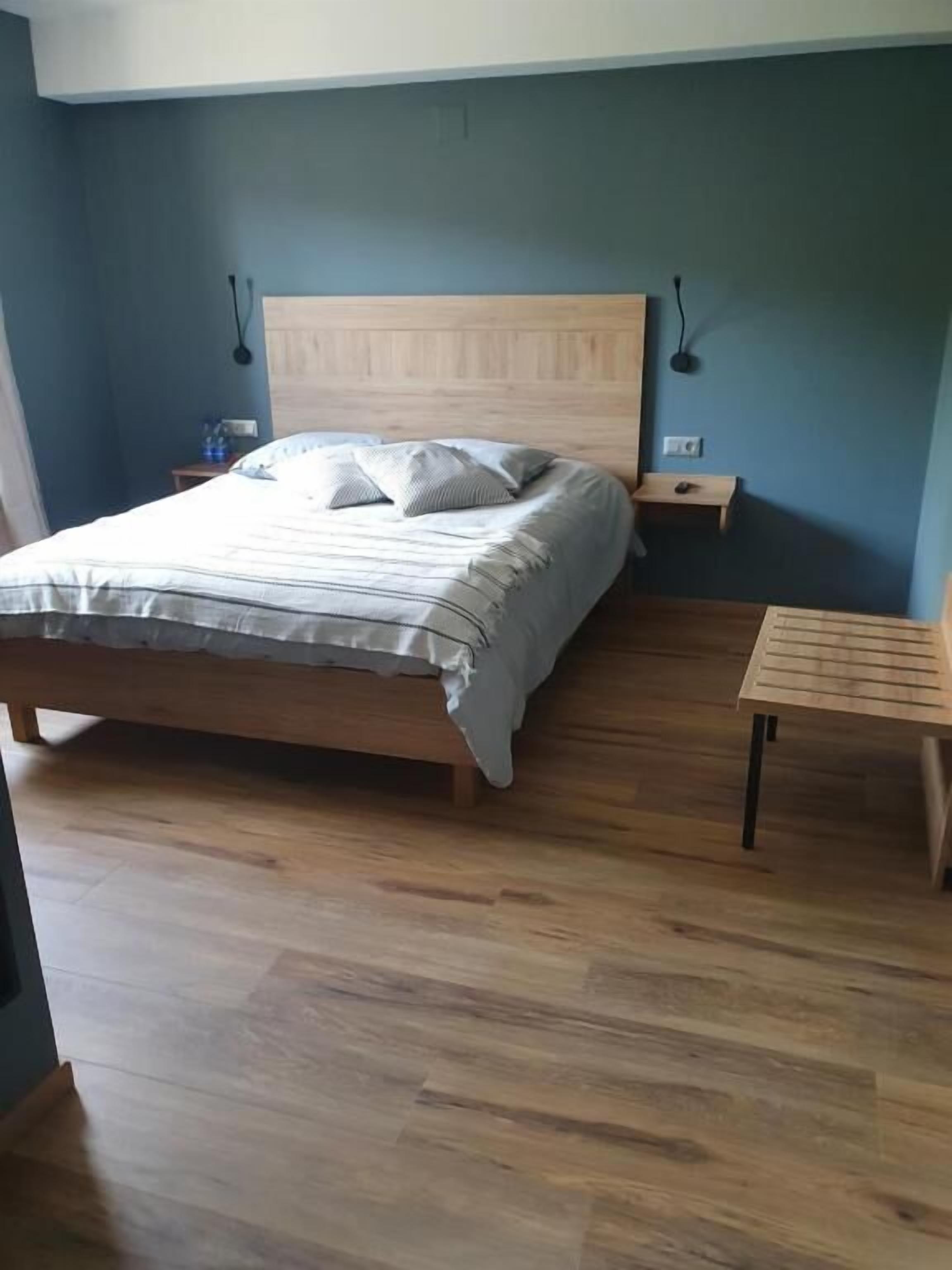 Un dormitorio con una cama de madera, una mesita de noche y una pequeña mesa de madera.