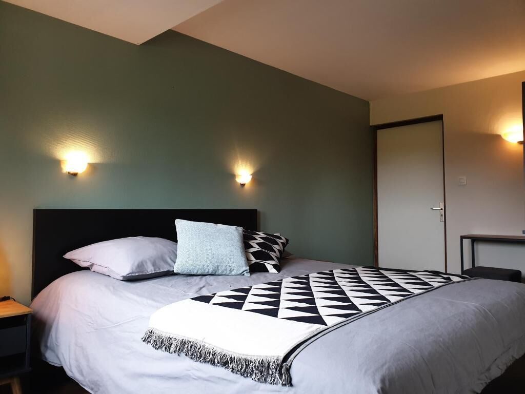 Una cama bien hecha con una manta de estampado geométrico, dos almohadas y una mesita de noche con una lámpara.