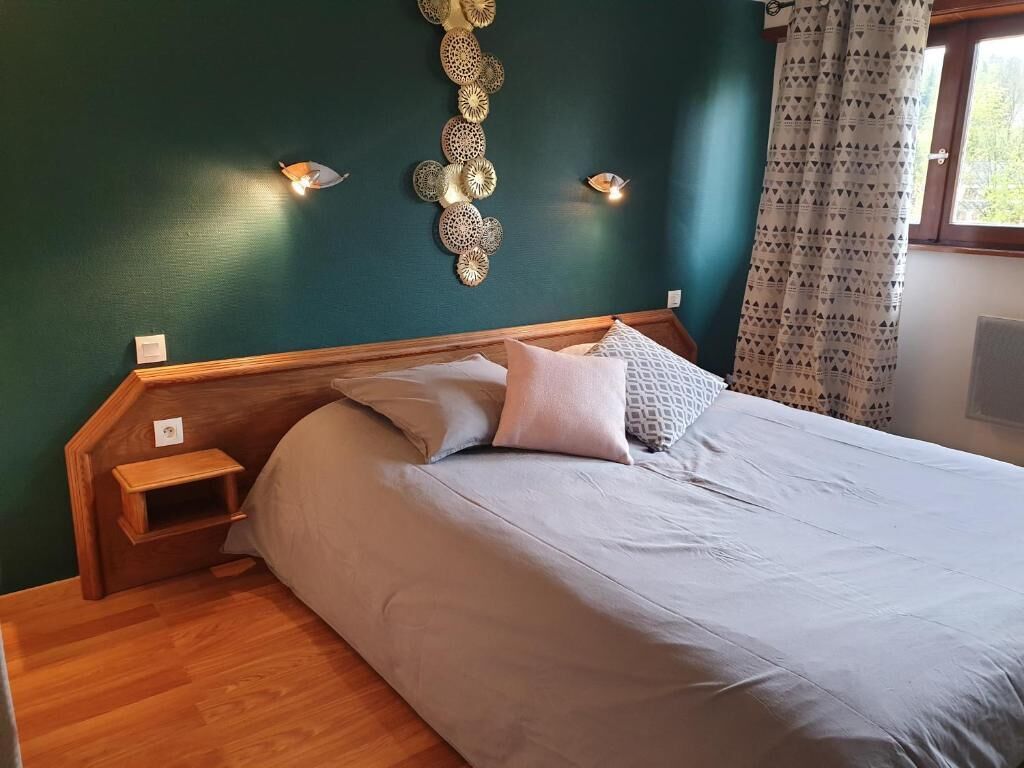 A bedroom with a bed, wooden nightstands, a wall-mounted light fixture, and a window with curtains.