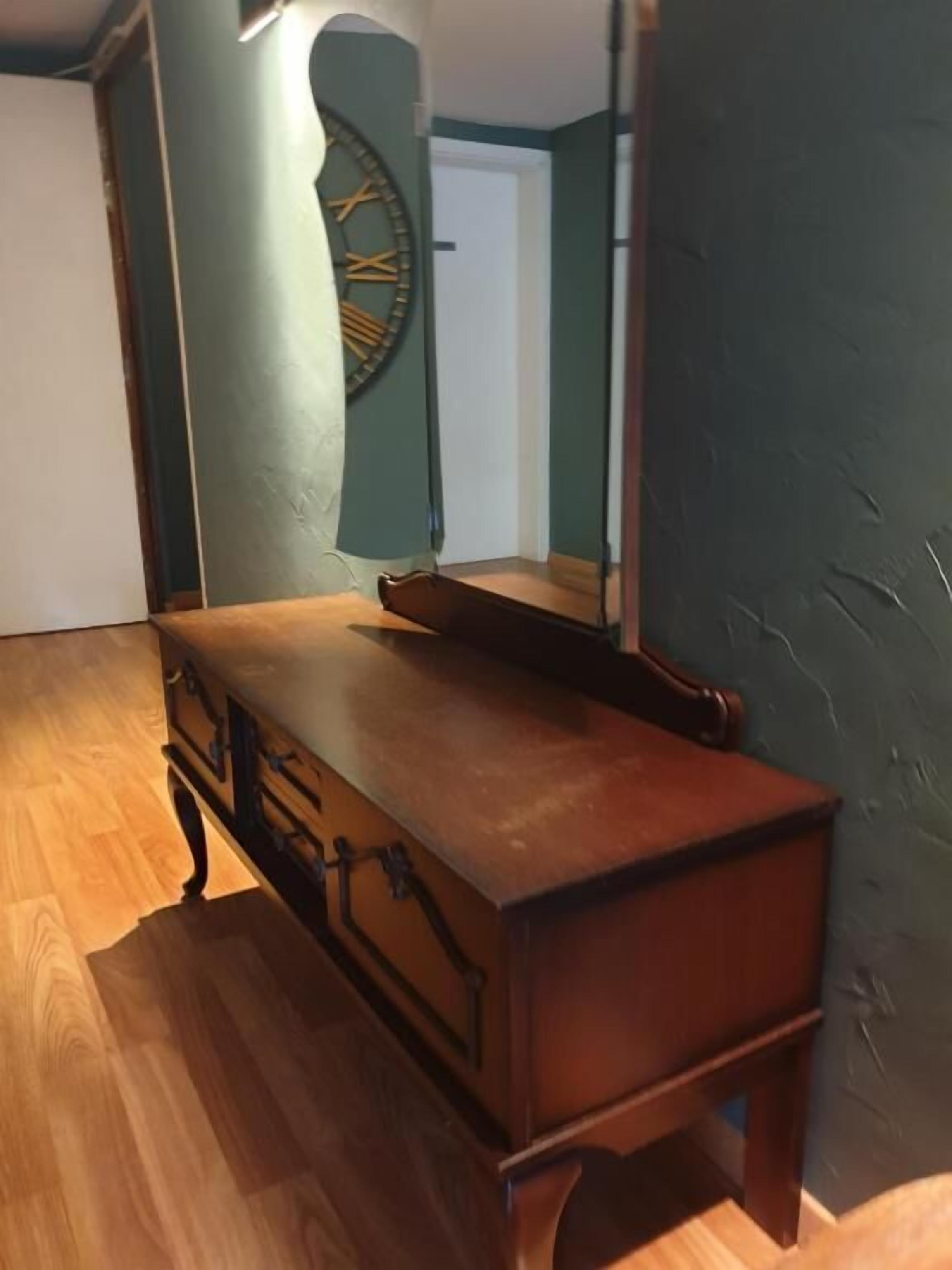 A wooden dresser with drawers and a mirror in a room with wooden flooring and a green accent wall.