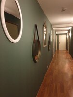 Un pasillo con paredes verdes, piso de madera y varios espejos y marcos de cuadros.