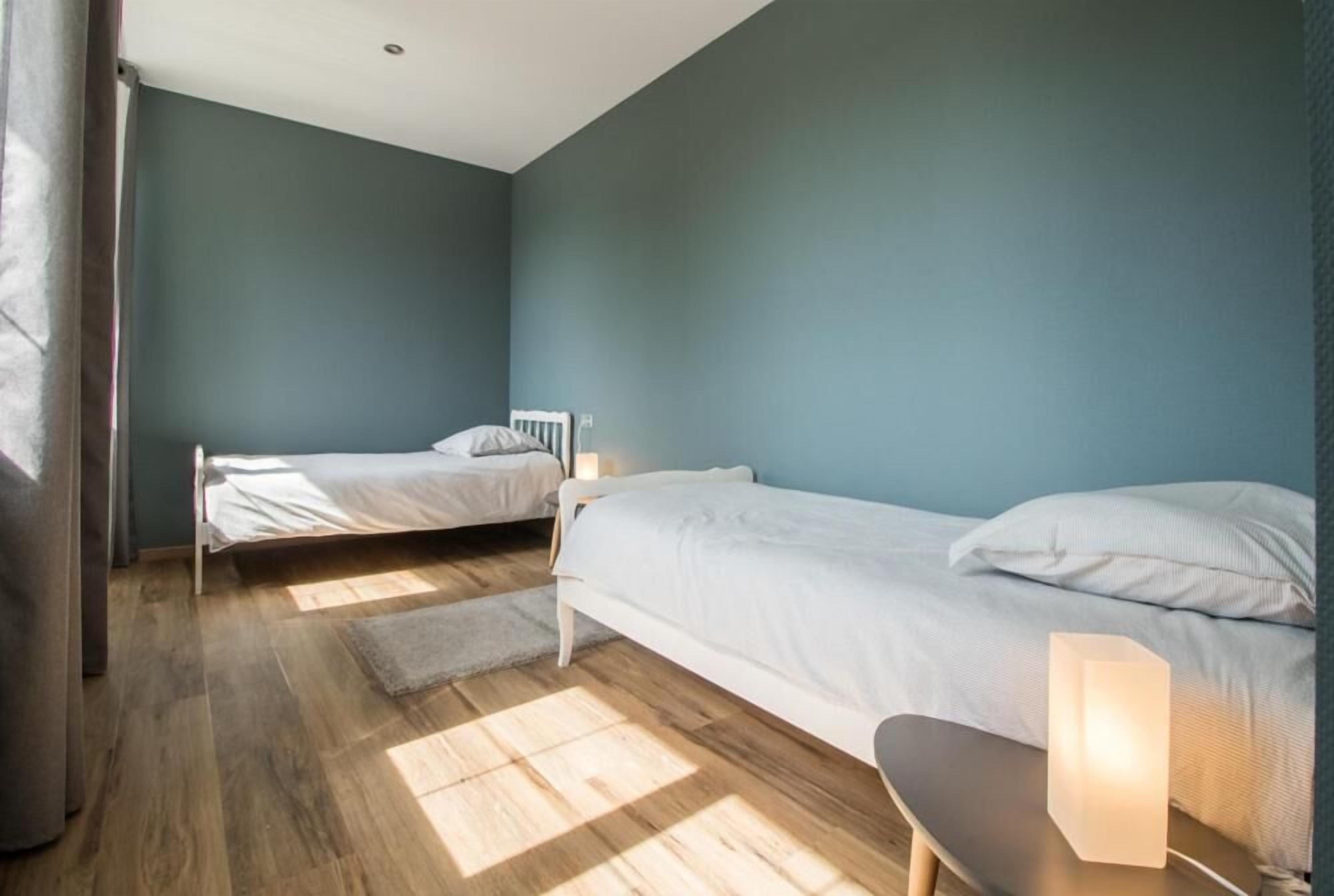 A bedroom with two beds, a bench, and a bedside table with a lamp.