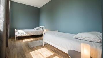 A bedroom with two beds, a bench, and a bedside table with a lamp.