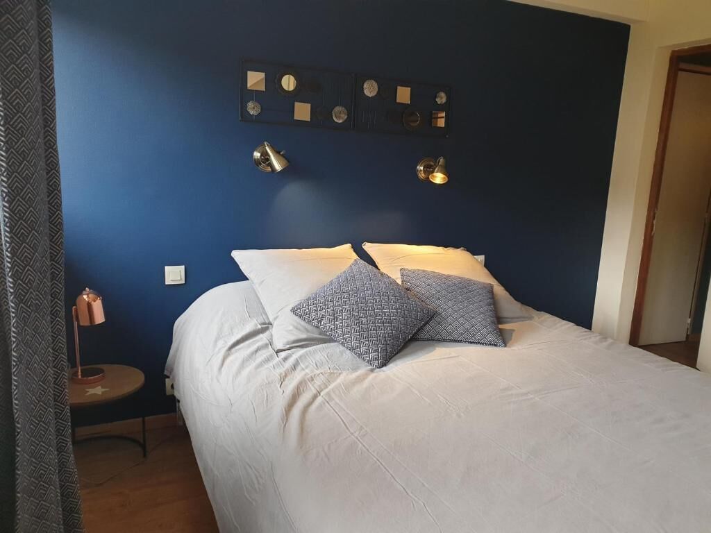 A bedroom with a bed, two bedside lamps, a wall clock, and a small table with a lamp.