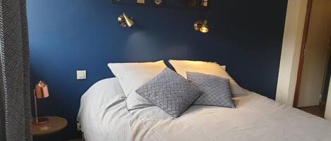 A bedroom with a bed, two bedside lamps, a wall clock, and a small table with a lamp.