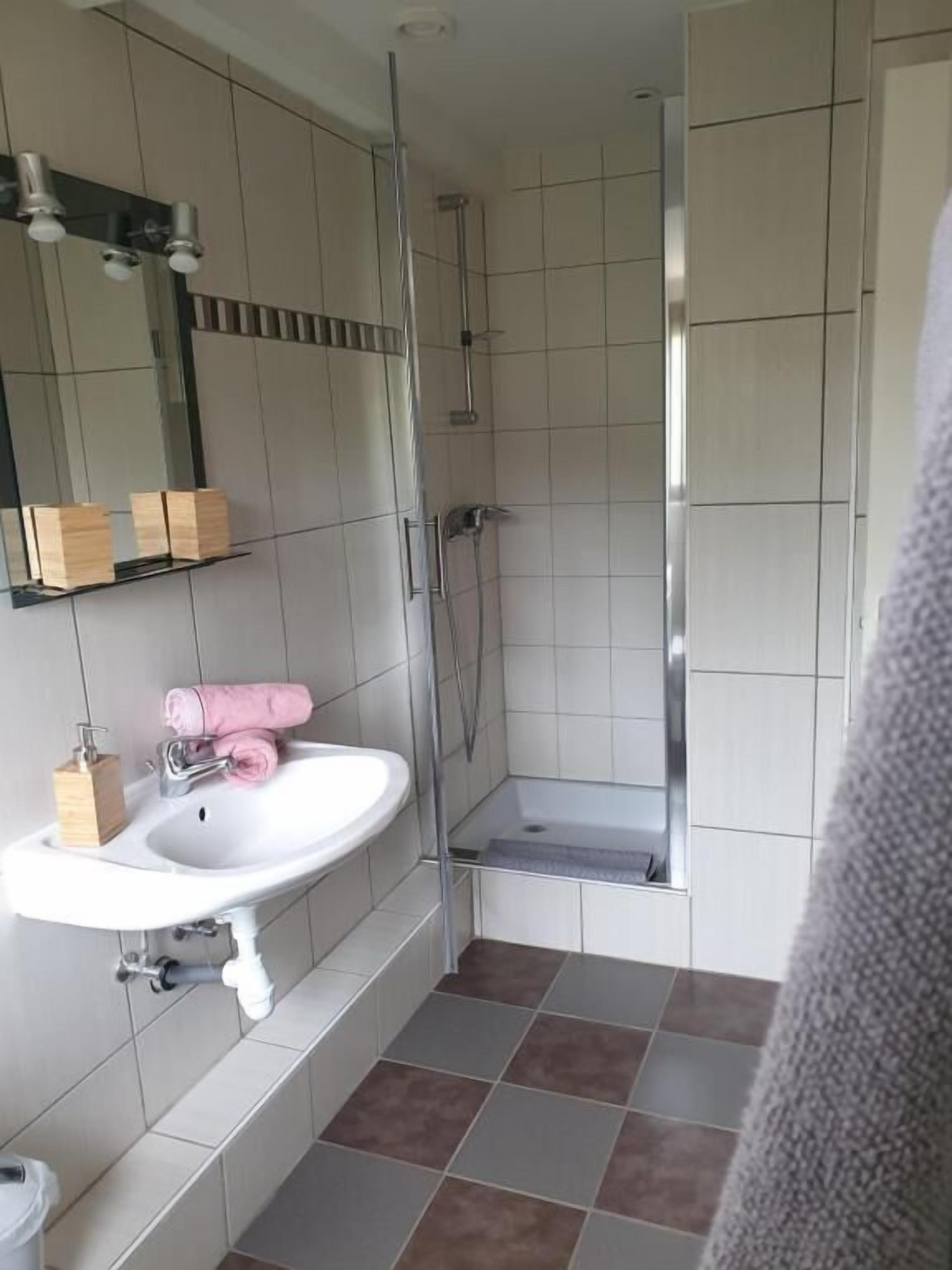 A bathroom with a white sink, a mirror, a shower, and a tiled floor.