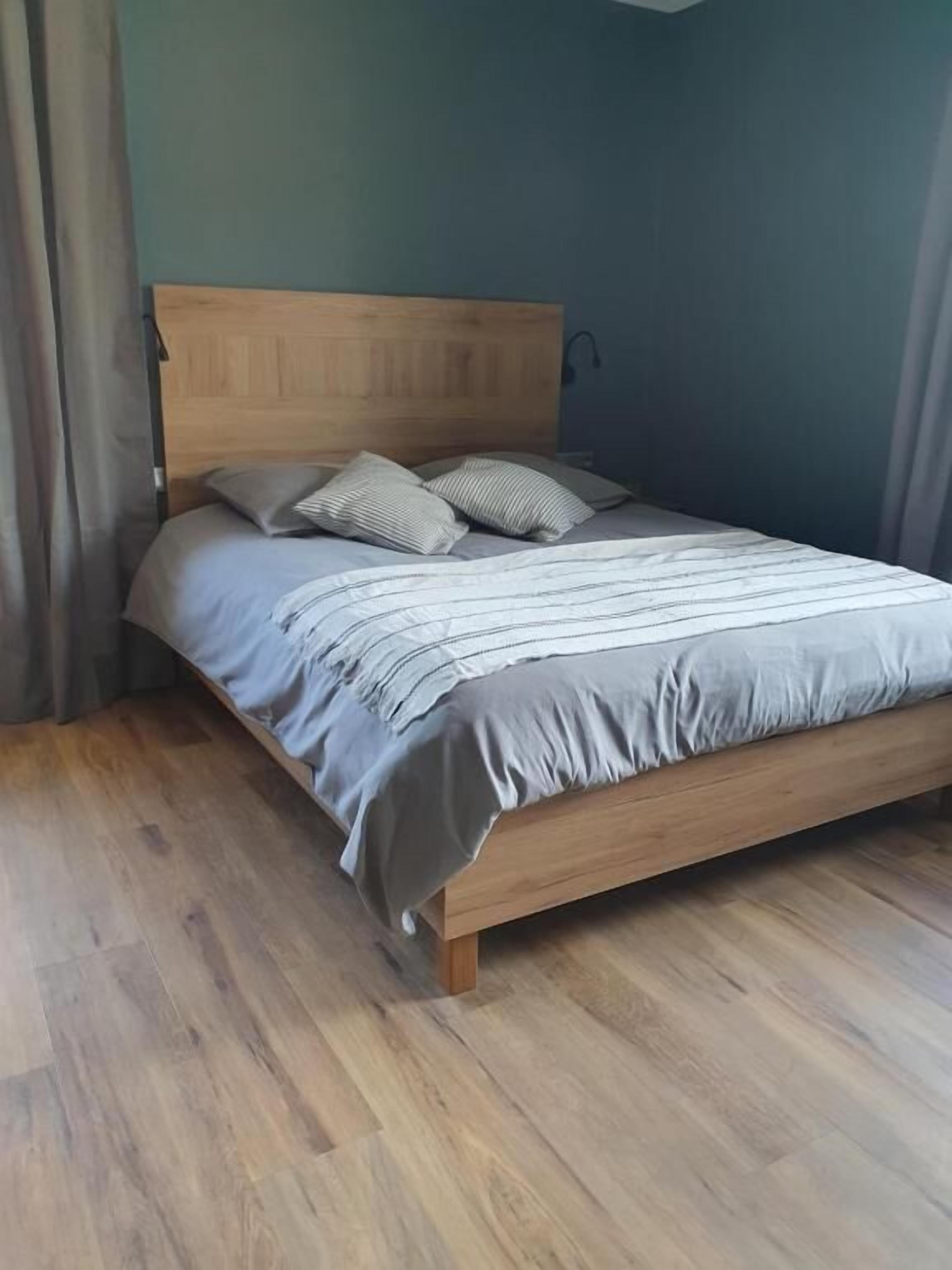 A bed with a wooden headboard, grey bedding, and two pillows.