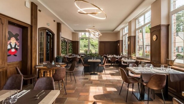 A restaurant with a modern interior, featuring wooden paneling, large windows, and a mix of table and booth seating. - Au Wingenerhof (Wingen-sur-Moder)