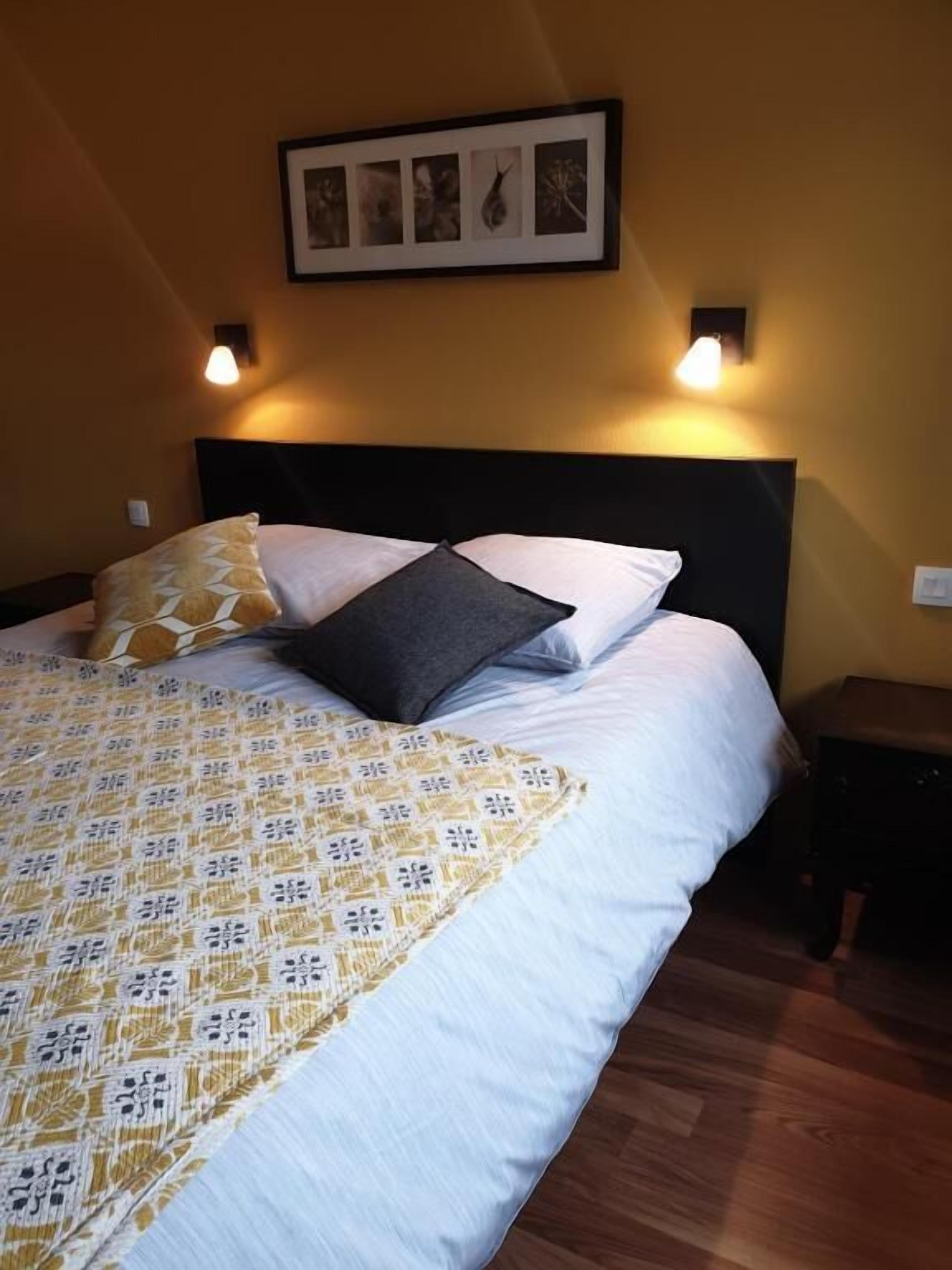 A neatly made bed with patterned bedding, a dark headboard, and two wall-mounted lamps.