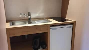 Una kitchenette compacta con un lavamanos, un refrigerador pequeño y una alacena con una tetera y tazas.