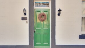 Eine grüne Tür mit einem Kranz, begleitet von zwei an der Wand befestigten Laternen, und ein kleines Fenster darüber.