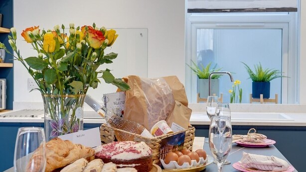 Ein Esstisch ist reichhaltig gedeckt, mit Speisen, einem Blumenstrauß und einem modernen Gemälde an der Wand.