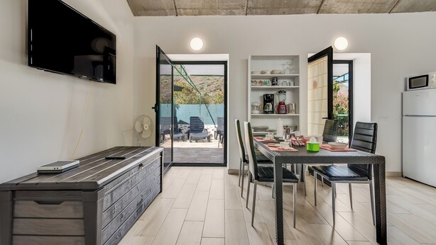 Eine moderne Küche mit Essbereich, einem an der Wand montierten Fernseher und Blick ins Freie.