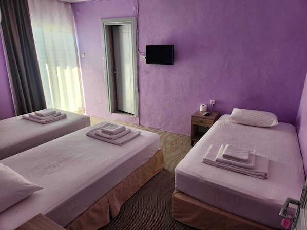 Une chambre d’hôtel avec deux lits, un téléviseur fixé au mur, une fenêtre avec des rideaux et une petite table de chevet avec une télécommande.