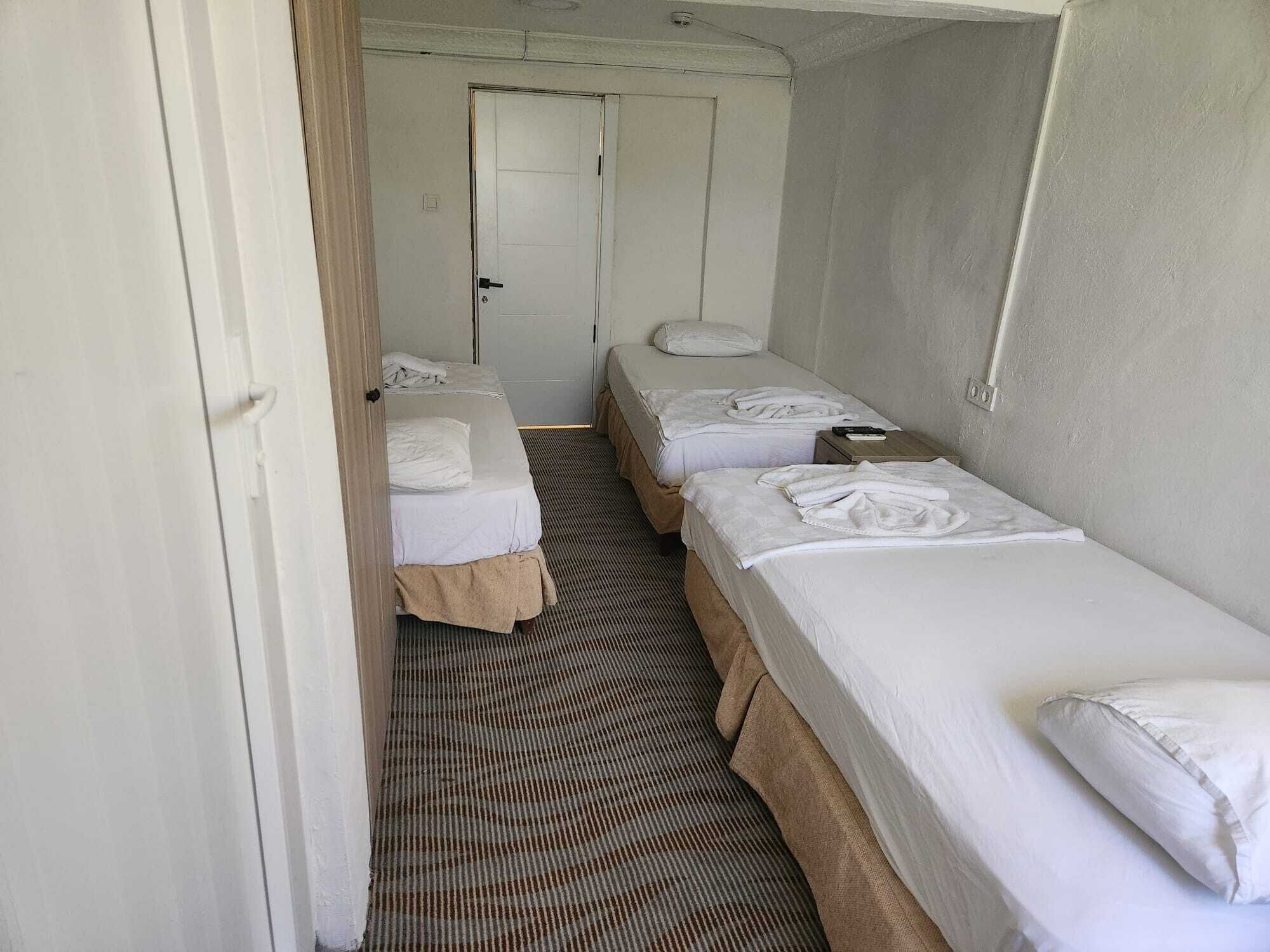 A narrow hallway leading to a room with two single beds, a door, and a striped carpet.