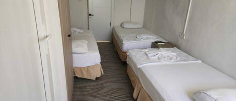 A narrow hallway leading to a room with two single beds, a door, and a striped carpet.