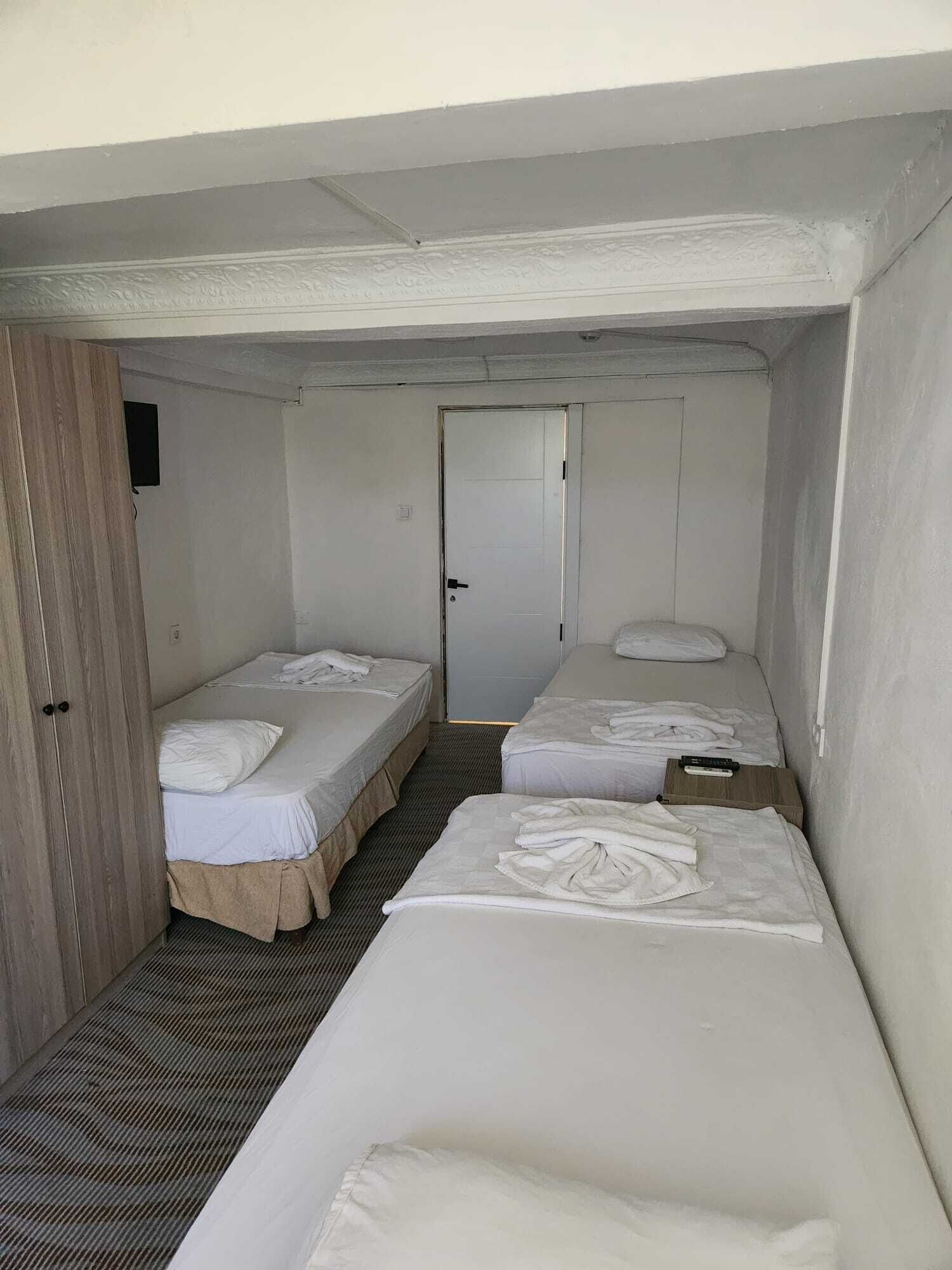 A small, compact room with two single beds, a door, and a wooden wardrobe.