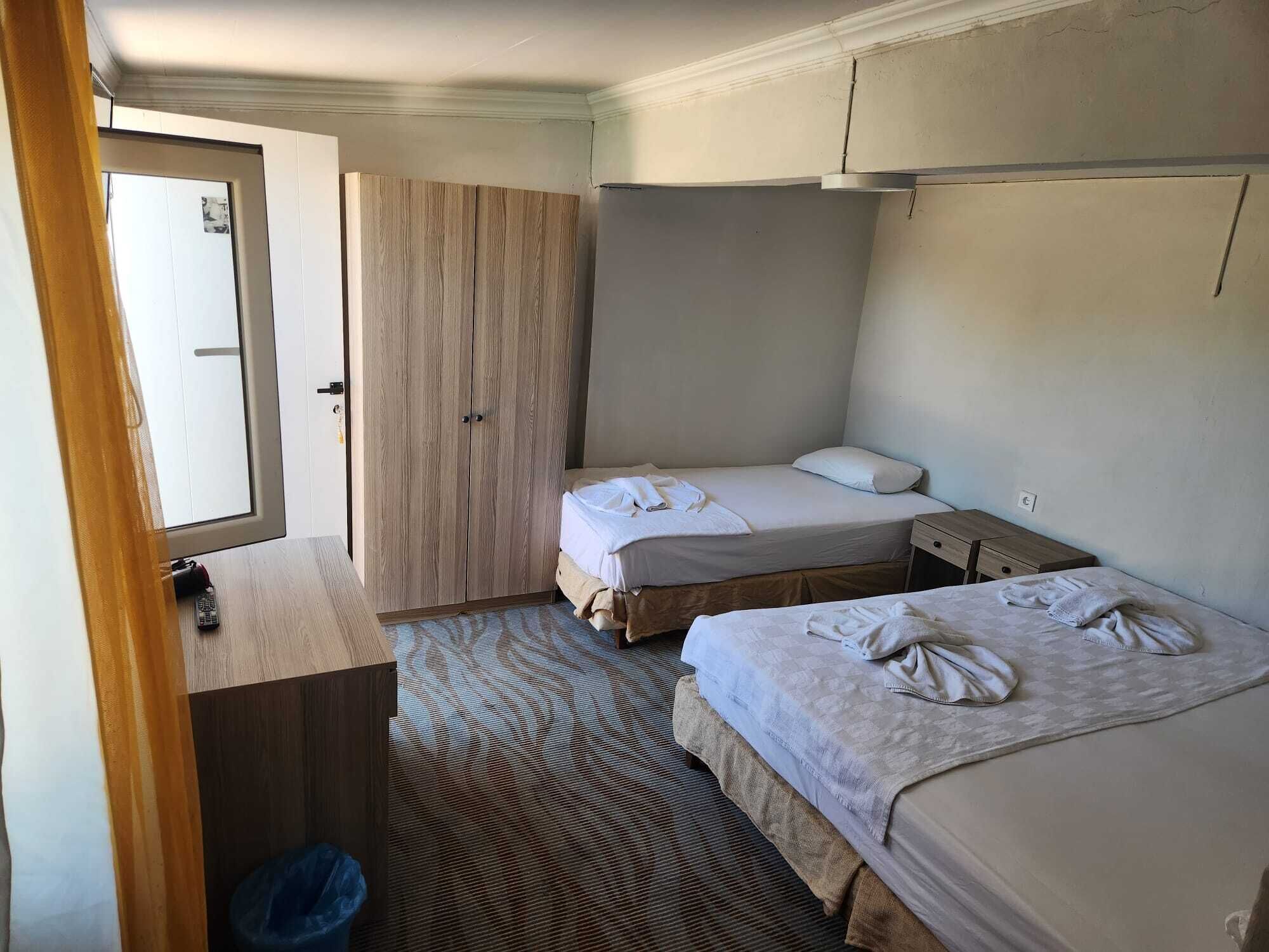 Habitación de hotel pequeña con dos camas, un armario de madera, un escritorio pequeño y una ventana.