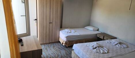 Habitación de hotel pequeña con dos camas, un armario de madera, un escritorio pequeño y una ventana.