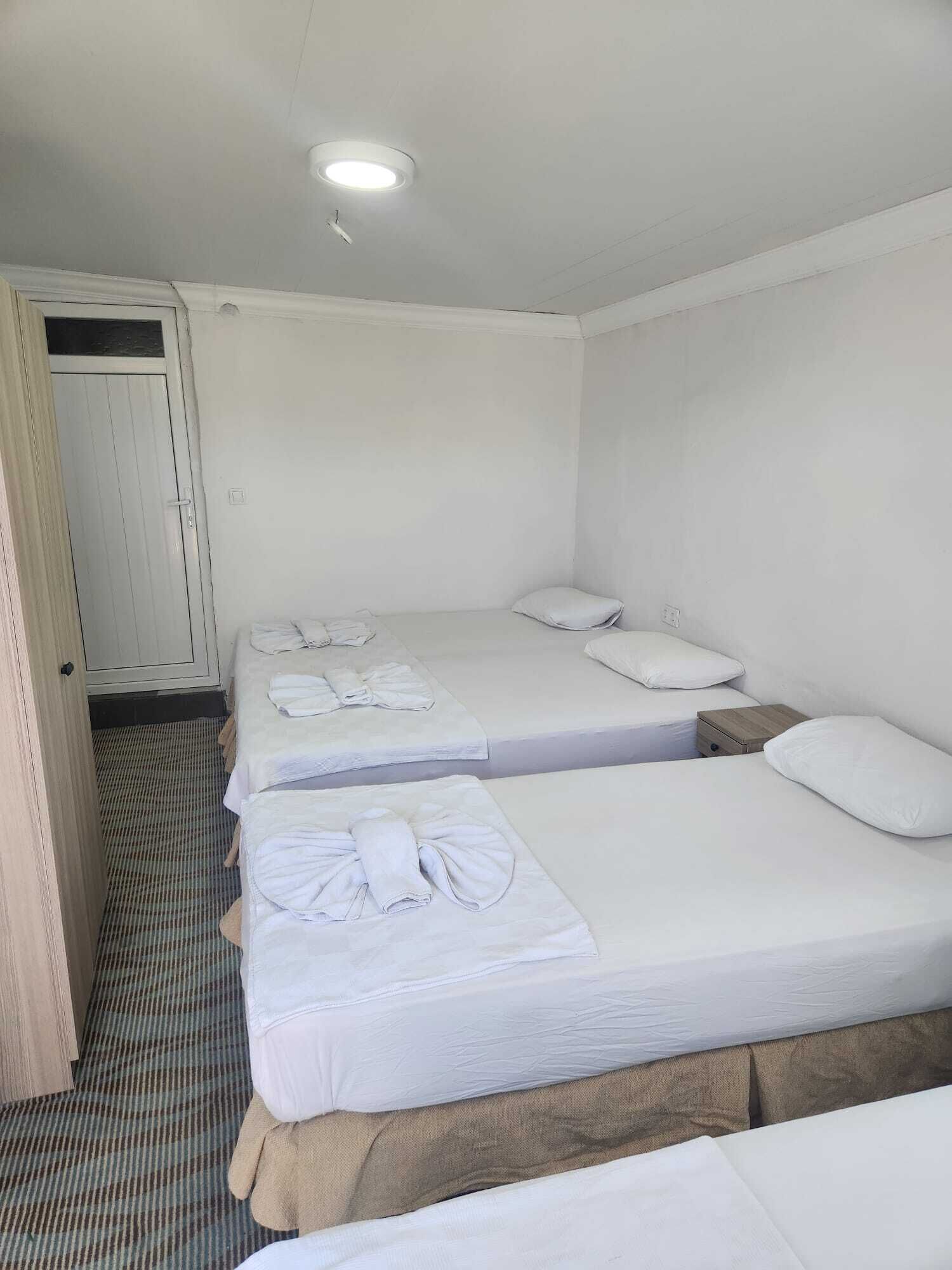 A hotel room with two single beds, a door, and a ceiling light.
