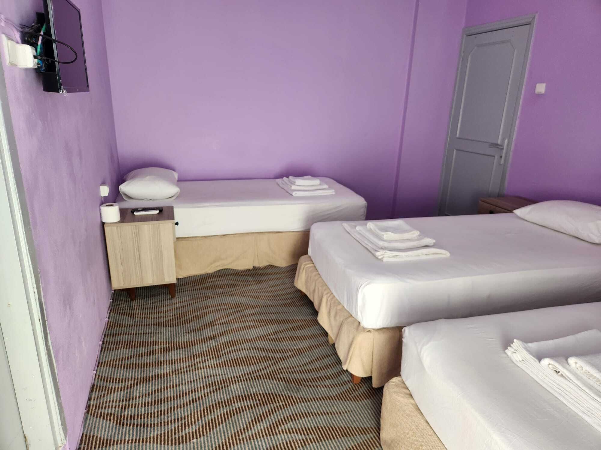 A room with two beds, a small bedside table, a wall-mounted TV, and a door.