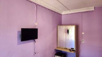 Una habitación con paredes moradas, un televisor montado, un mueble de madera con espejo y un pequeño cubo de basura.