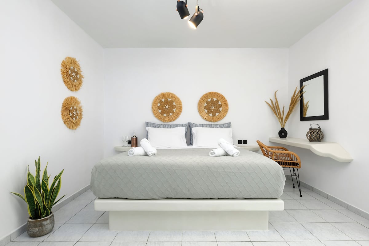 Quarto moderno com uma cama grande, duas decorações circulares na parede, uma mesa de cabeceira, uma cadeira e um pequeno vaso de planta.