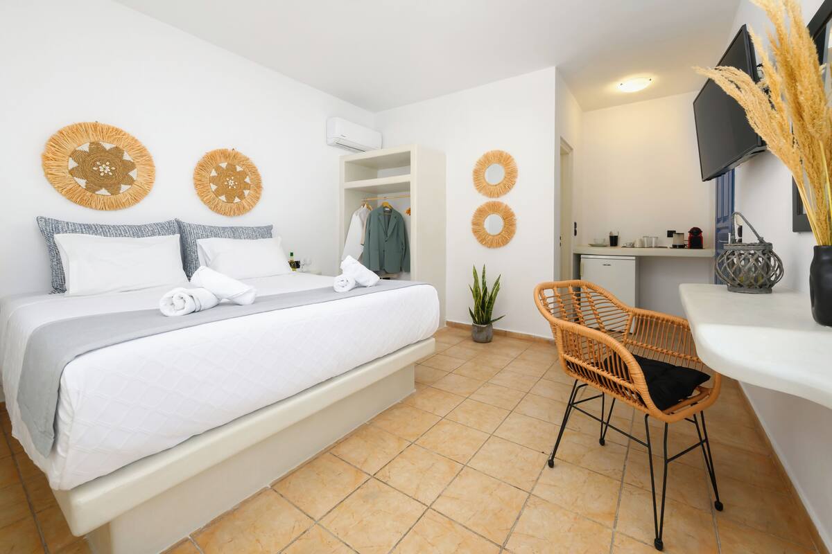 Quarto moderno com cama, mesa de cabeceira, uma cadeira e um pequeno espaço de cozinha.