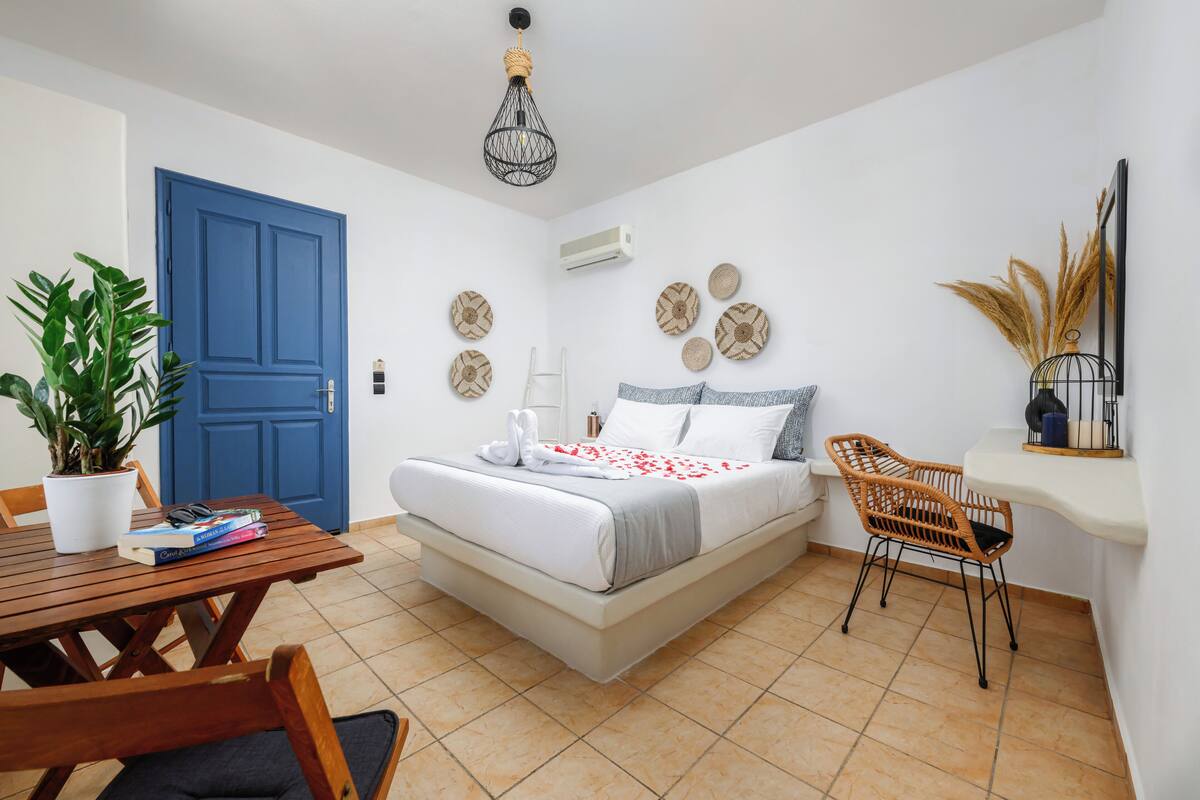 Quarto com cama, escrivaninha, cadeira, planta em vaso e porta azul.
