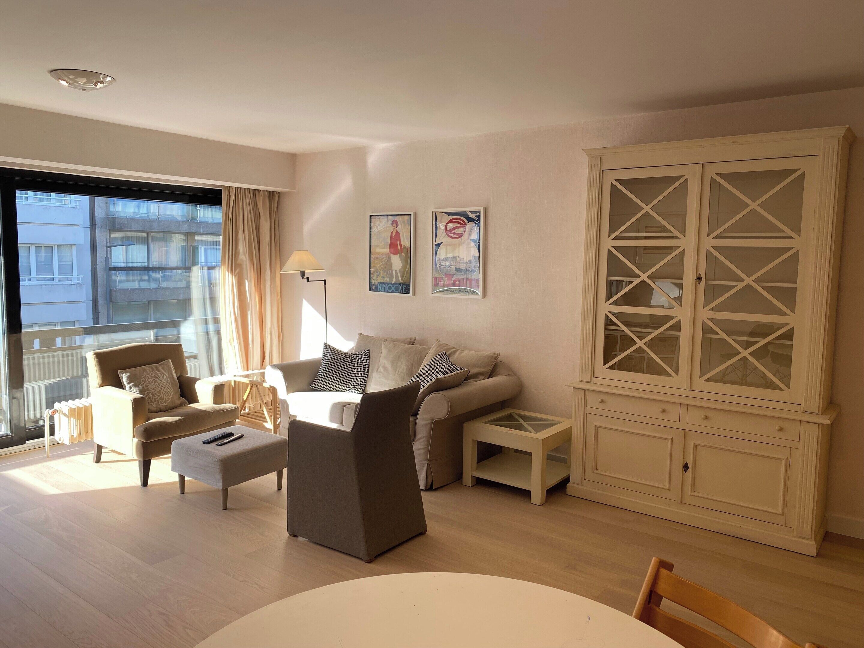 A living room with a sofa, armchairs, a coffee table, a cabinet with glass doors, and a view of the outside.