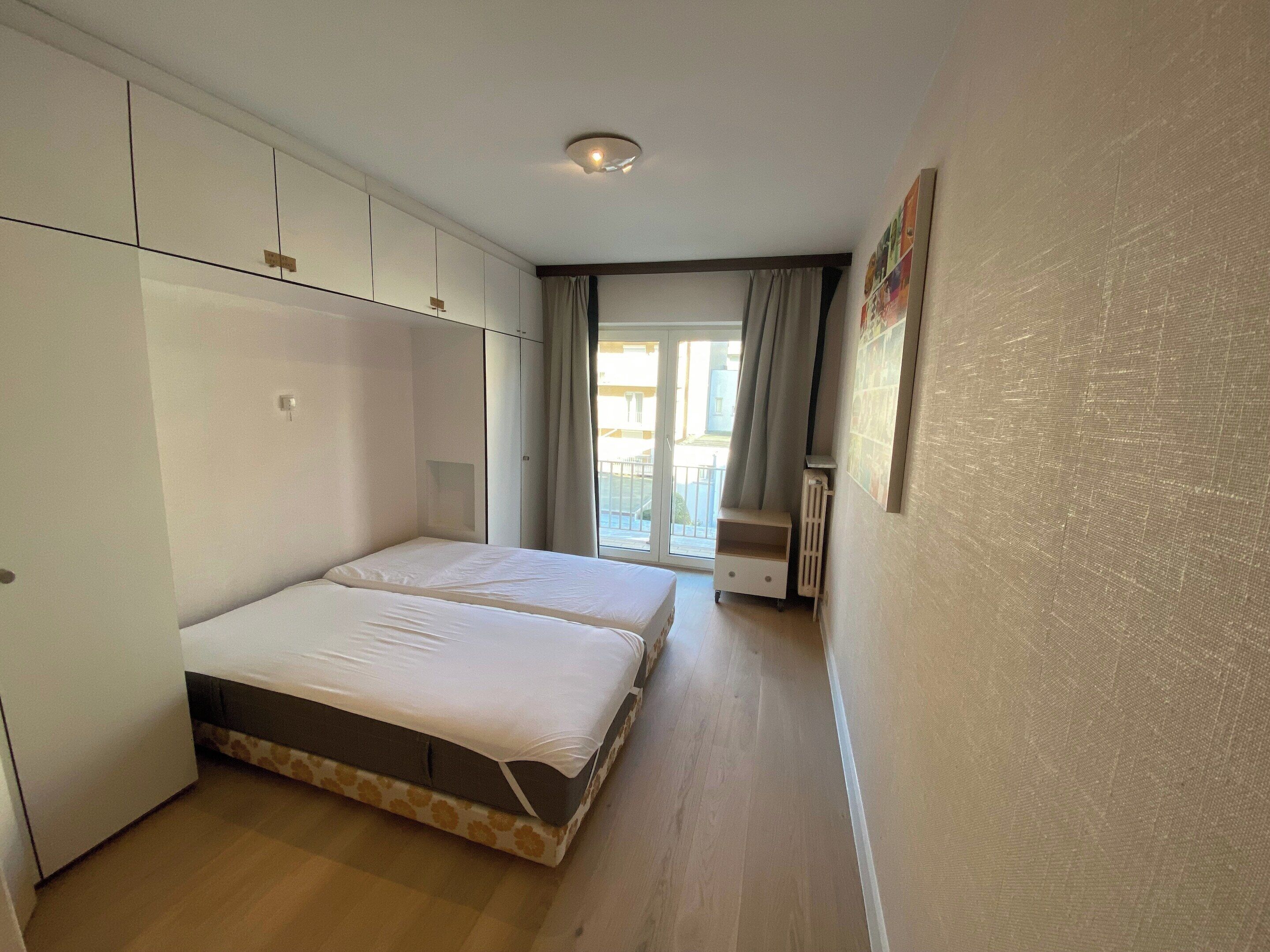 A bedroom with a bed, wardrobe, and a view of the outside.