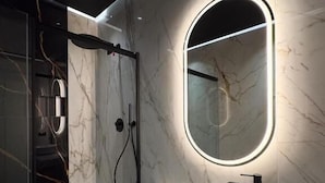 Ein modernes Badezimmer mit Marmorwand, einem runden Waschbecken und einem Spiegel mit beleuchtetem Rahmen.