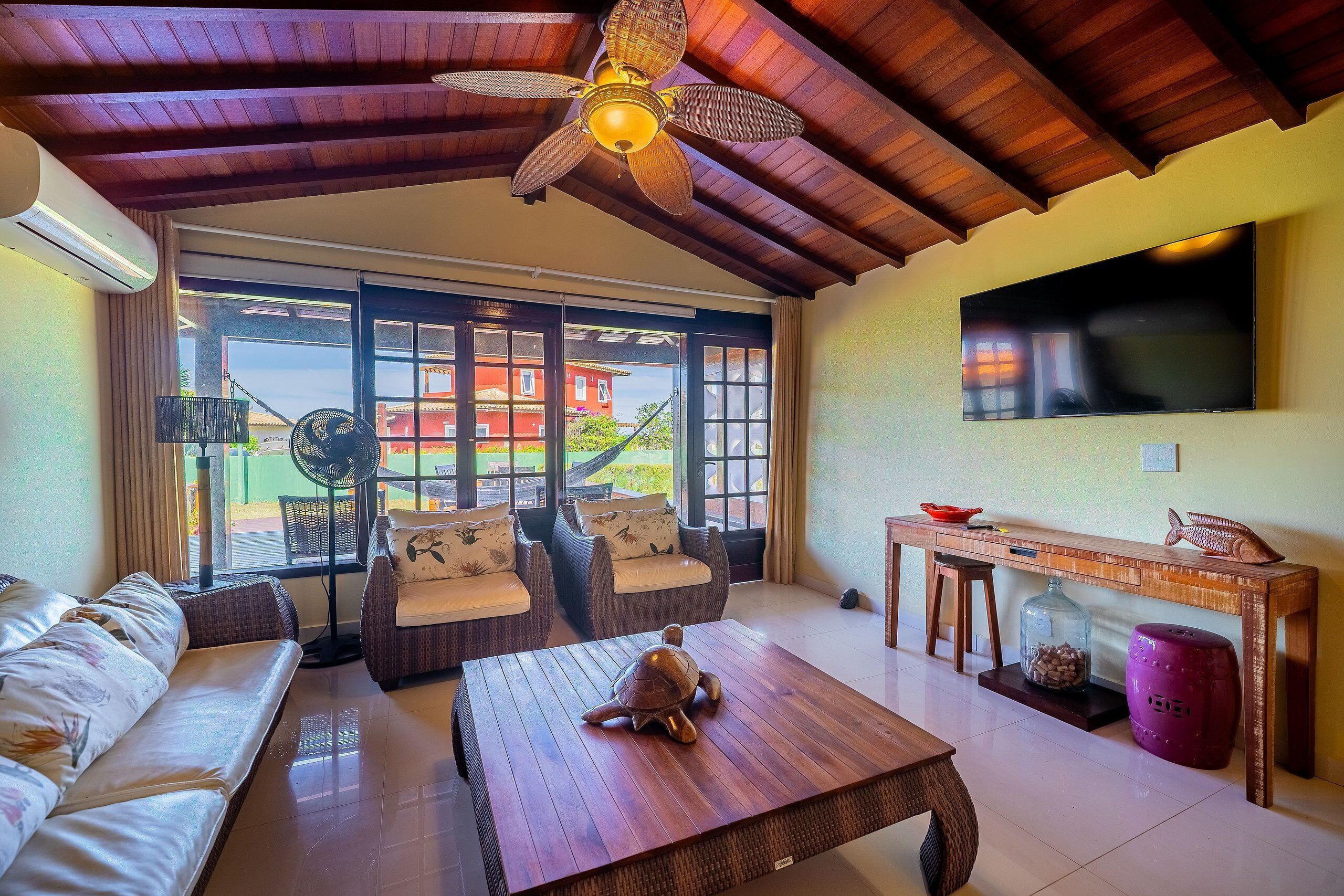 A spacious living area with a ceiling fan, a large flat-screen TV, a wooden coffee table with a turtle decoration, and a sofa.