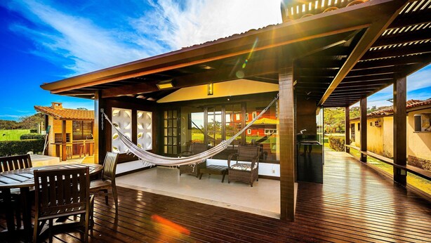 A covered outdoor patio with wooden flooring, a hammock, and outdoor furniture. - Bz60 Casa em condomínio pé na areia (Buzios)