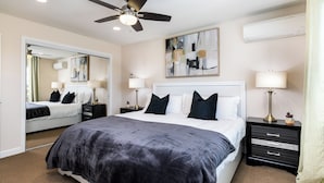 A hotel room with a large bed, a ceiling fan, a mirror, two bedside tables with lamps, and a wall-mounted air conditioner. - Peaceful & Gated 2 King Bd 2 Bth, 1 Gig WiFi near CLU, FSAC & Proactive Sports (Thousand Oaks)