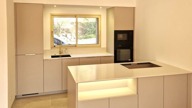 A modern kitchen with a central island, built-in appliances, and a window providing natural light.