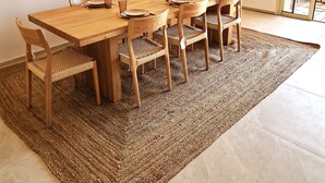 A dining area with a wooden table and chairs, a woven rug, and a vase with flowers.