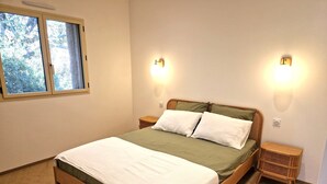 A neatly made bed with a green and white bedspread, two bedside tables with lamps, and a window with a view of trees.