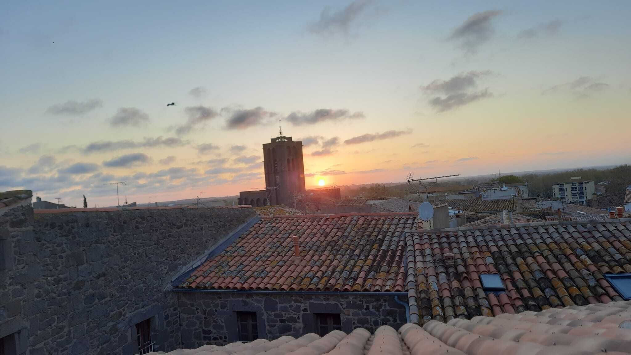 A stone building with a tiled roof, a tower, and a sunset in the background.