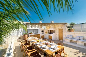 An outdoor dining area with a stone wall, a built-in grill, and a seating bench.