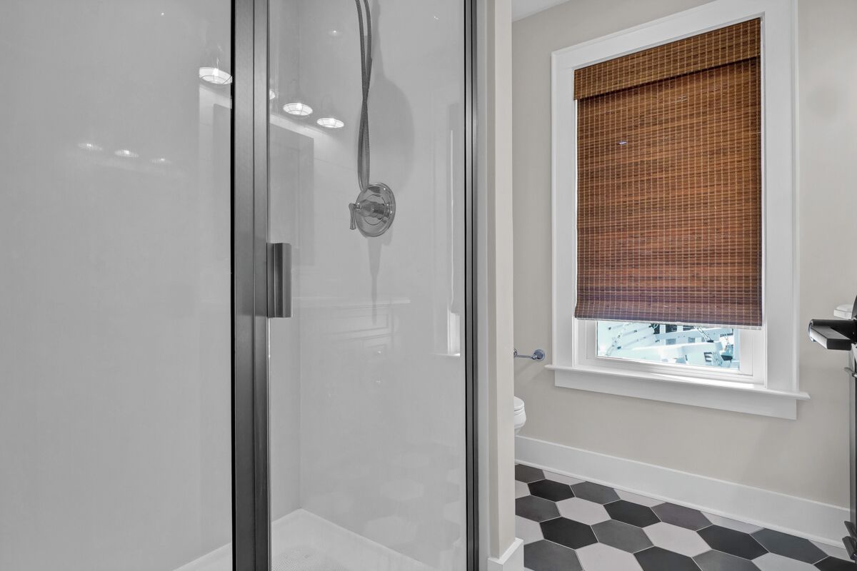 Ein modernes Badezimmer mit einer Duschkabine aus Glas, einem Fenster mit einem Karokorb und einem schwarz-weißen Fliesenboden.