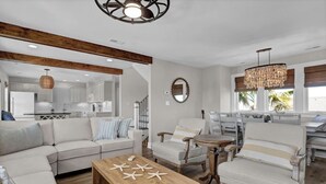 A spacious living room with a wooden coffee table, a sofa, and two armchairs. A kitchen is visible in the background. - Ocean & Sound Views, Elevator, Close to Beach & Dining! (Wrightsville Beach)