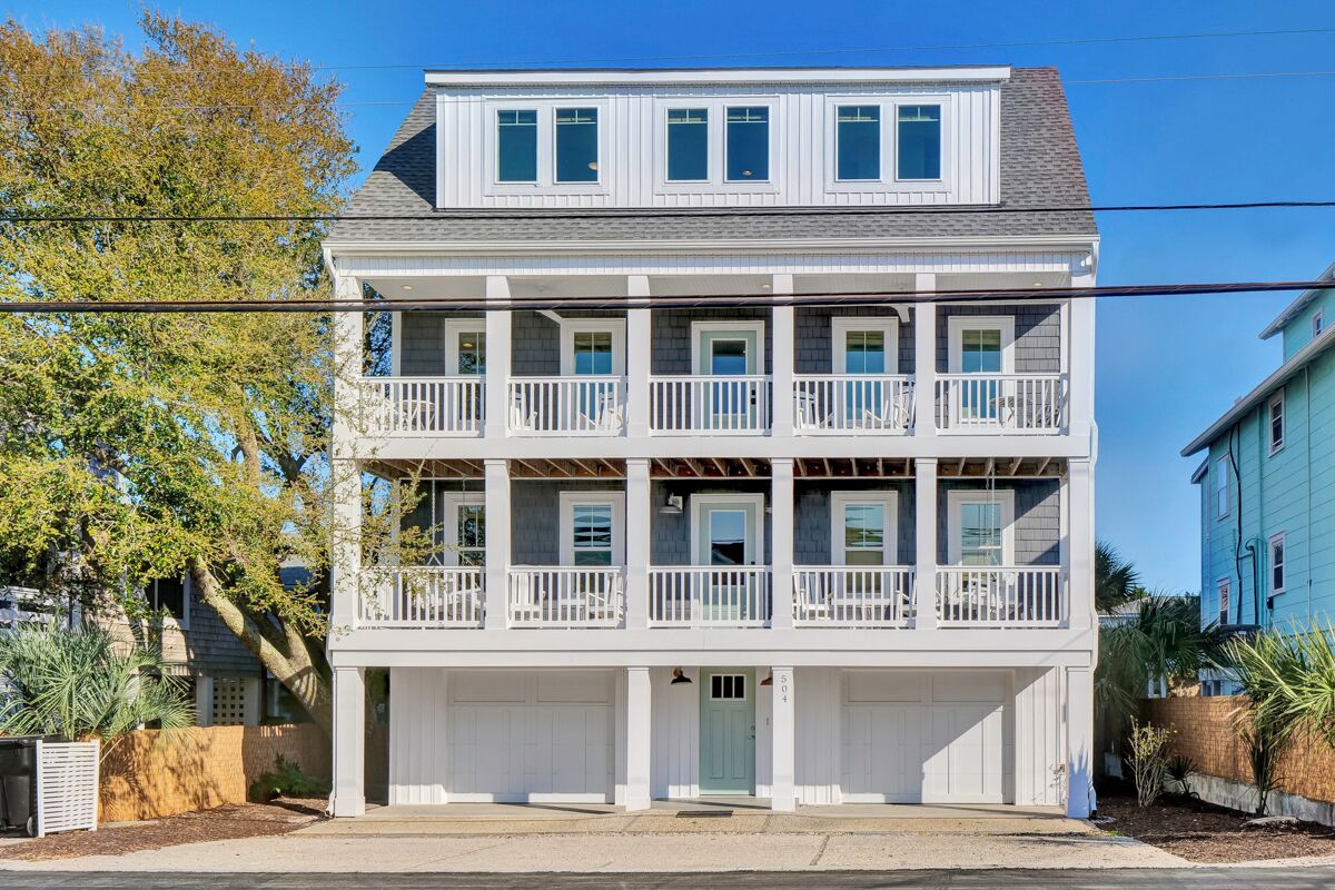 A two-story building with a balcony on each floor, a garage at the front, and a clear sky.