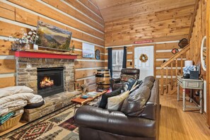 L’intérieur chaleureux d’un chalet avec une cheminée en pierre, un canapé en cuir et un plafond en bois.