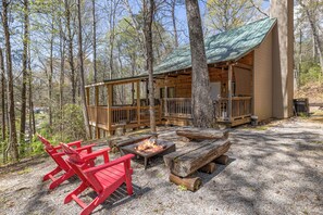 Une cabane avec une terrasse, un foyer extérieur et des fauteuils Adirondack rouges.