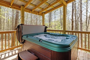 Een hottub op een houten terras, met uitzicht op een bos.